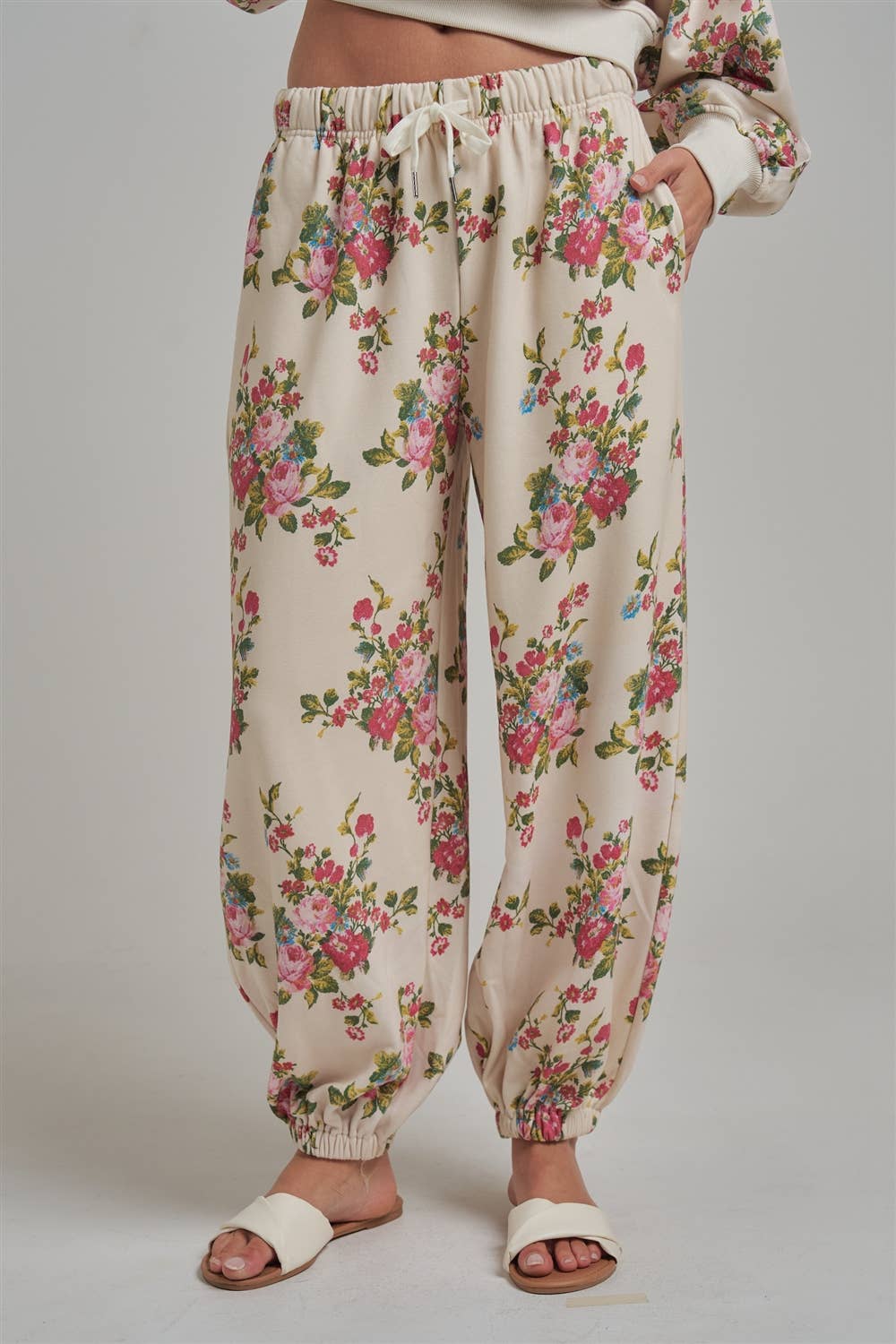 Floral patterned wide leg jogger sweat pants worn by a person with white sandals on a plain background