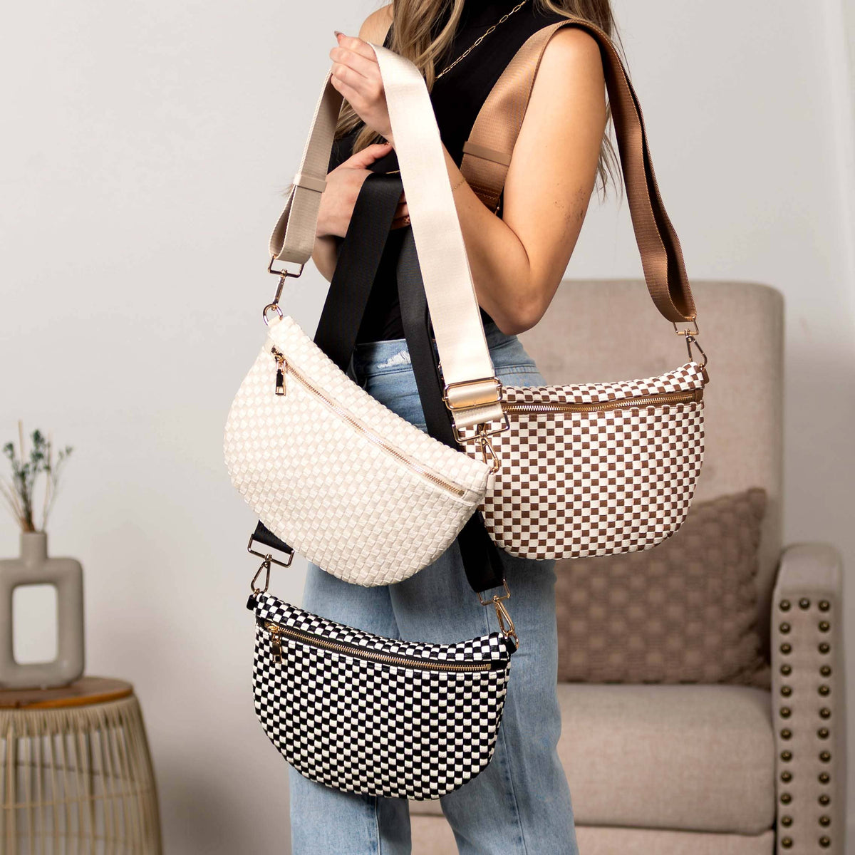 A woman models three woven crossbody and hip bags in different colorways: cream, brown-and-white checkered, and black-and-white checkered, shown in a styled indoor setting.