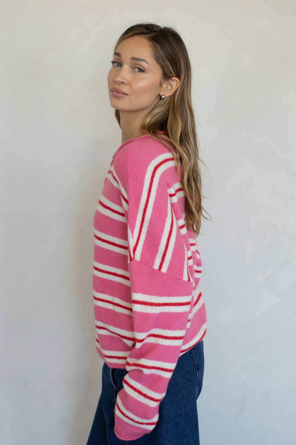 Woman wearing a pink, red, and white striped sweater against a plain background