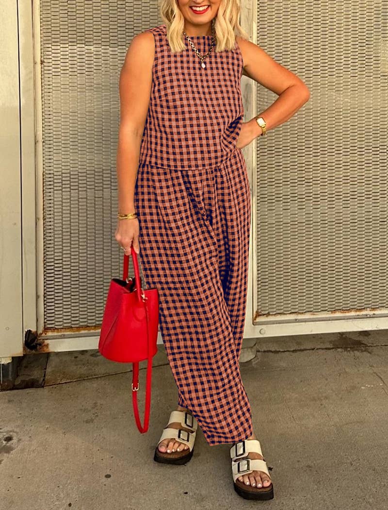 Woman wearing a matching red and brown checkered tank top and wide leg set with a red handbag against a textured wall.