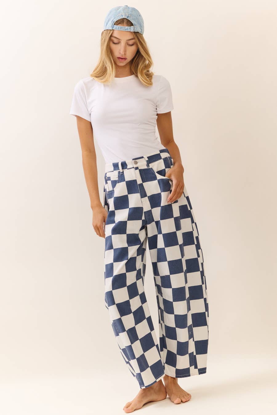 Woman wearing a white t-shirt and blue and white checkered barrel pants on a plain background
