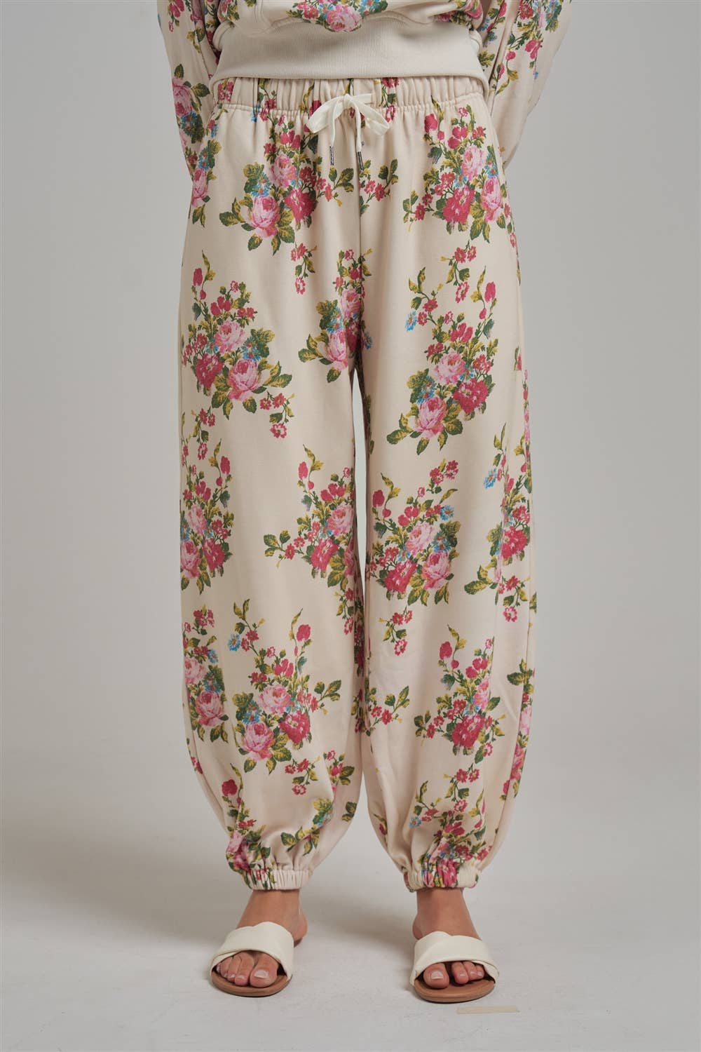Floral patterned wide leg jogger sweat pants worn by a person with white sandals on a plain background