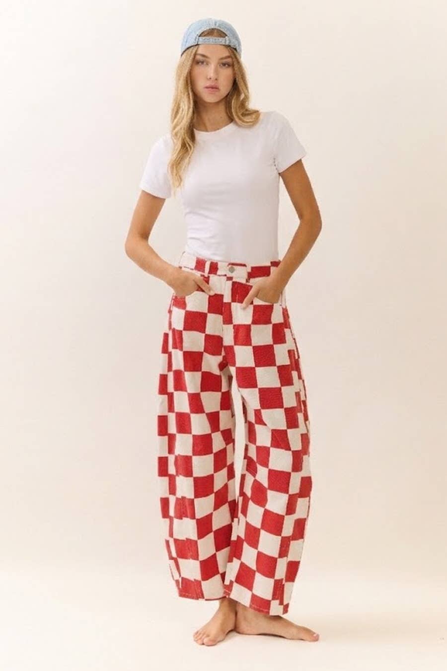 Woman wearing a white t-shirt and red and white checkered barrel pants on a plain background