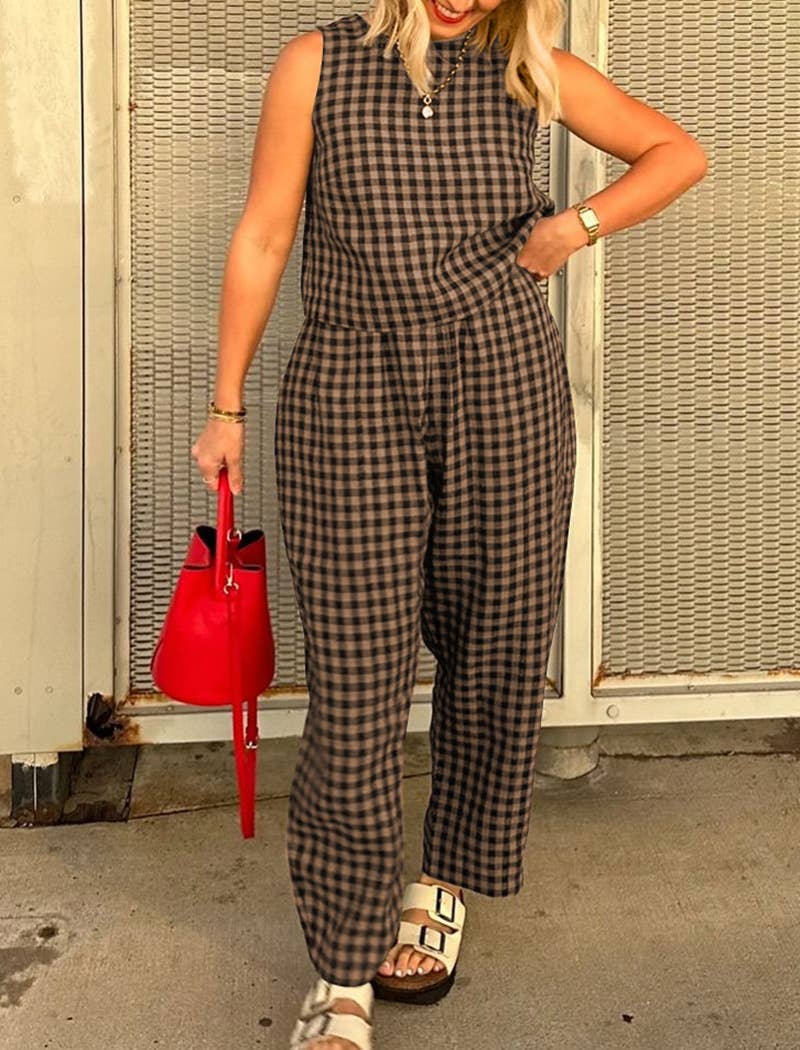 Woman wearing a matching brown and black checkered tank top and wide leg set with a red handbag against a textured wall.
