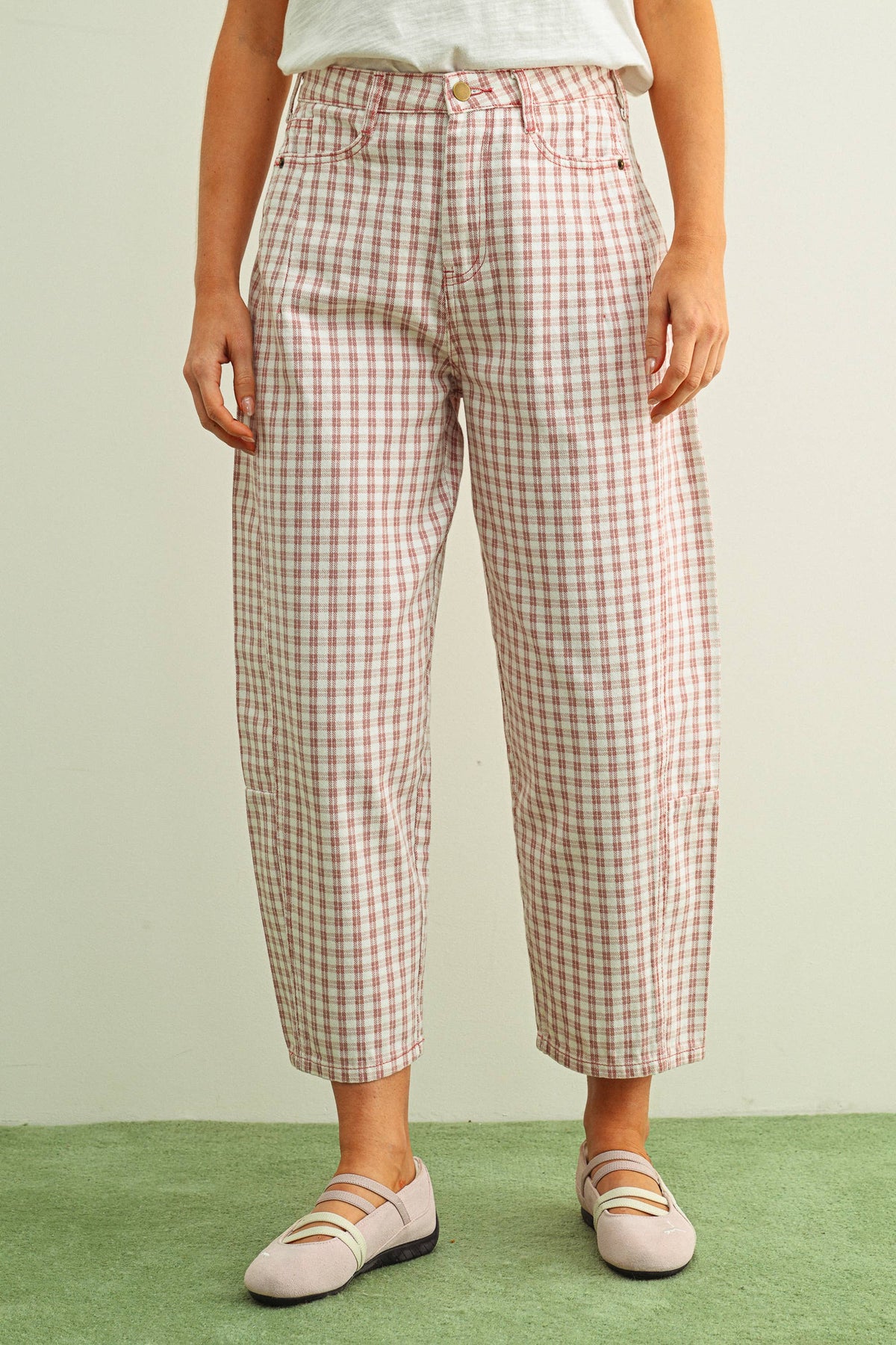 Person wearing pink and white checkered barrel pants and light pink shoes on a light green background
