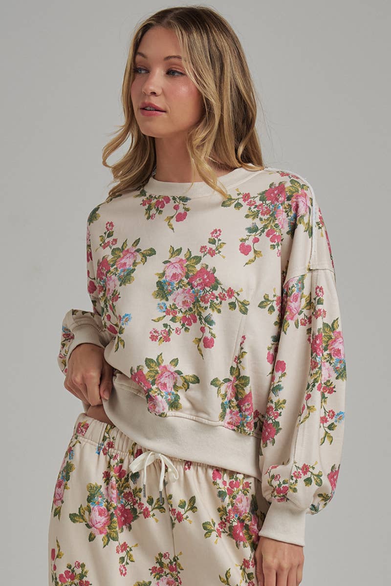 Woman wearing a floral long-sleeve pullover hoodie top and matching floral pants on a gray background