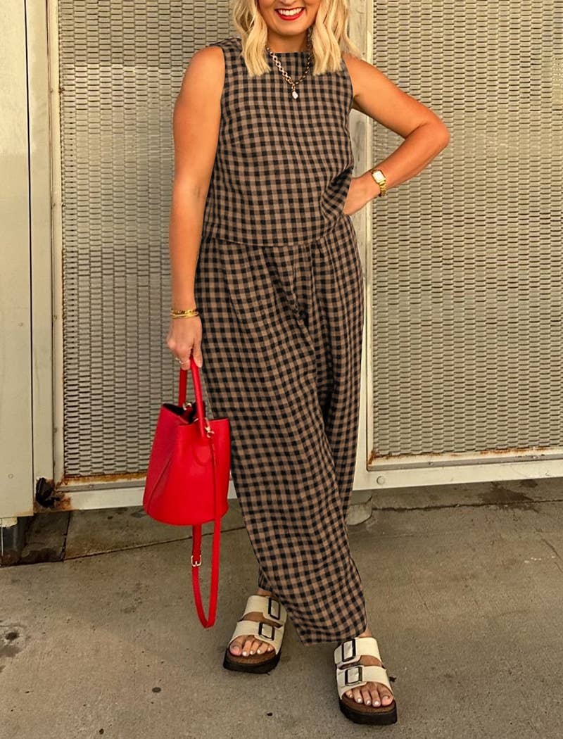 Woman wearing a matching brown and black checkered tank top and wide leg set with a red handbag against a textured wall.