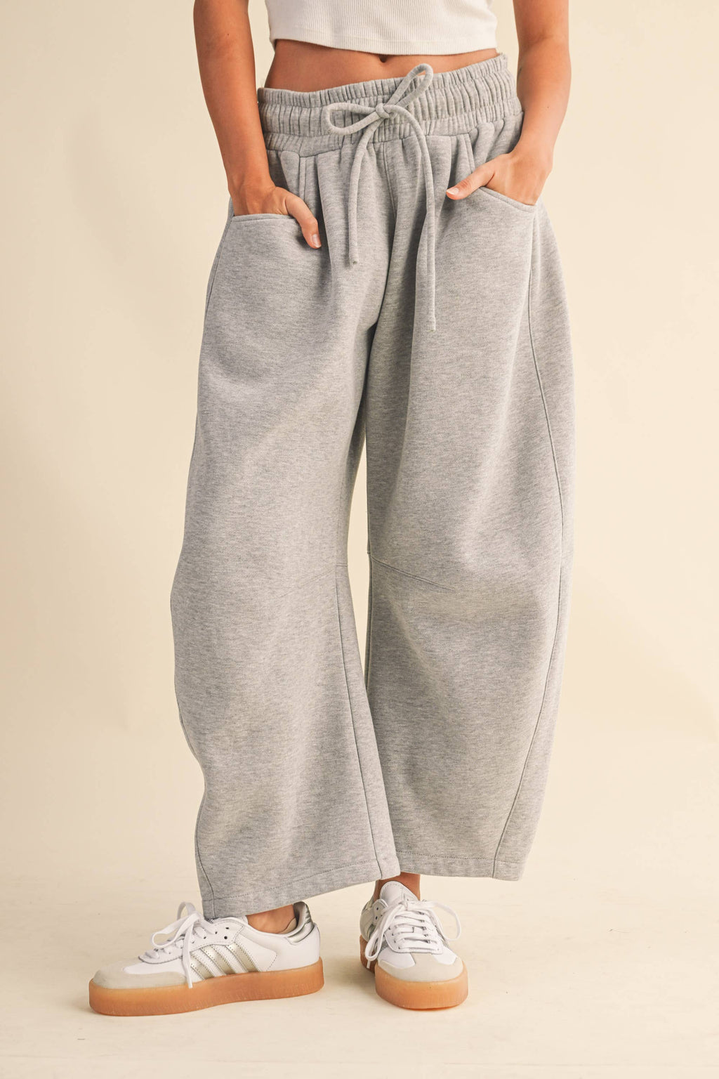 A person wearing light heather gray wide-leg barrel sweatpants with an elastic drawstring waist and side pockets, paired with white sneakers, against a plain beige studio background.