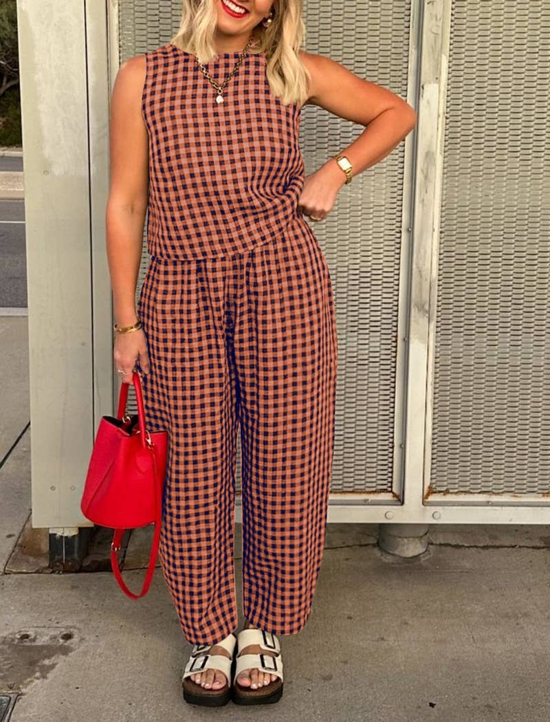 Woman wearing a matching red and brown checkered tank top and wide leg set with a red handbag against a textured wall.
