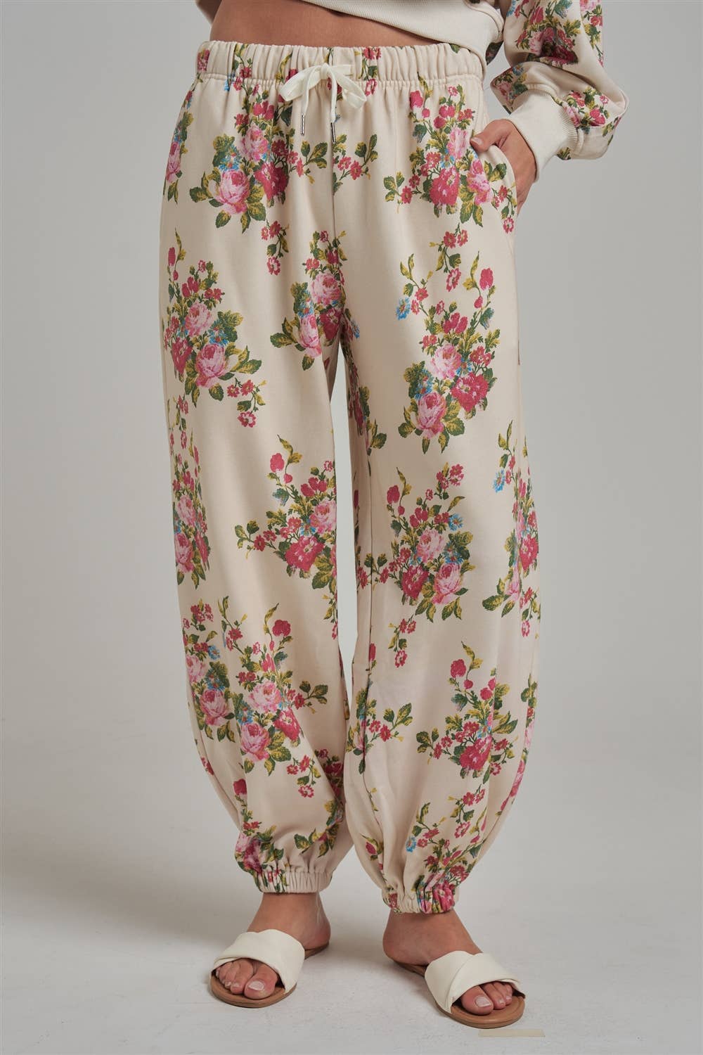Floral patterned wide leg jogger sweat pants worn by a person with white sandals on a plain background