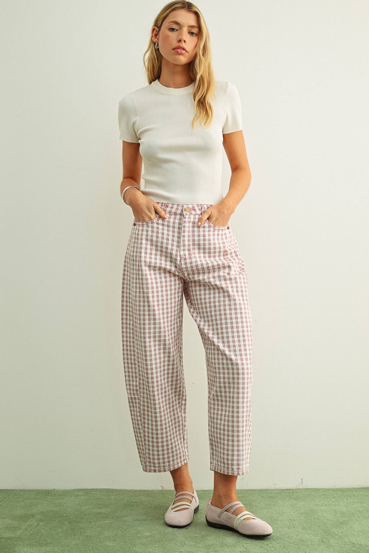 Woman wearing a white t-shirt and pink and white checkered barrel pants against a plain background