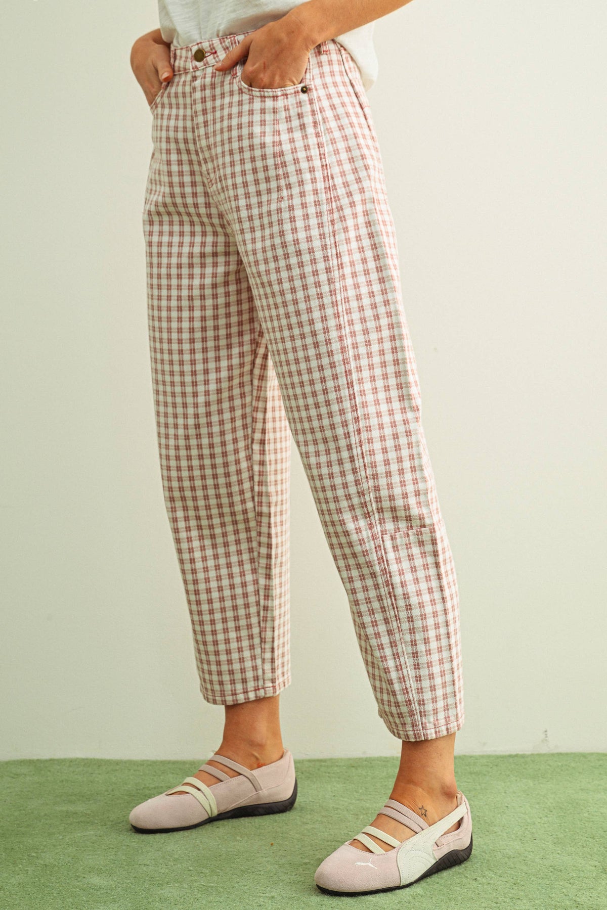 Person wearing pink and white checkered barrel pants and light pink shoes on a light green background