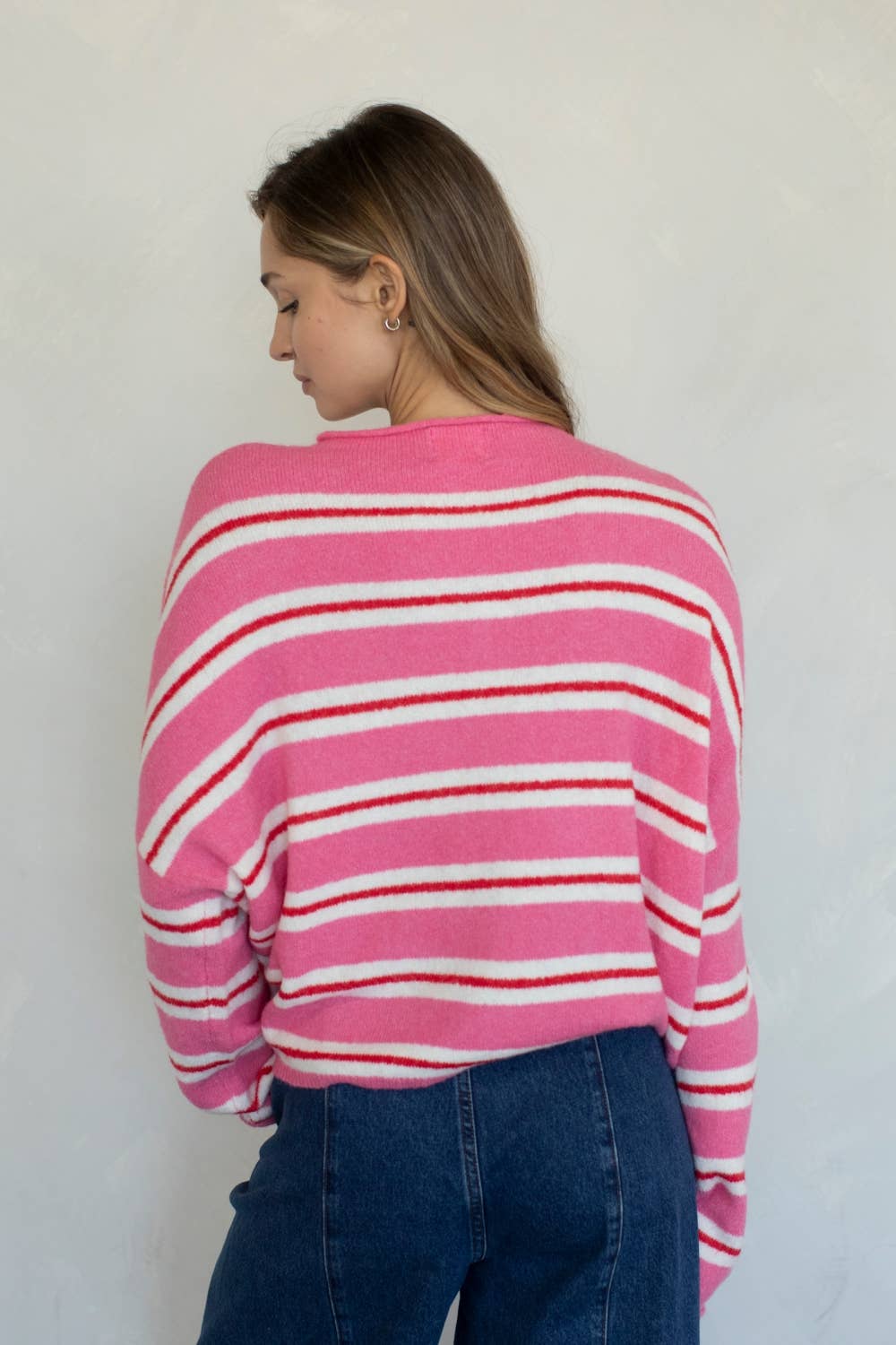 A woman model facing backwards, wearing a pink and white striped sweater against a plain background