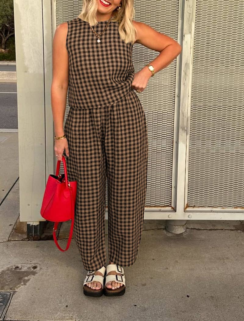 Woman wearing a matching brown and black checkered tank top and wide leg set with a red handbag against a textured wall.