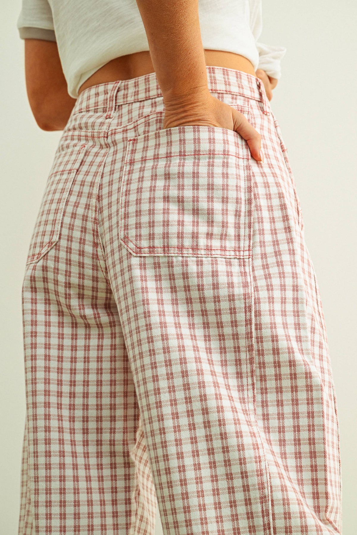 Person wearing pink and white checkered barrel pants with a hand in one pocket against a plain background