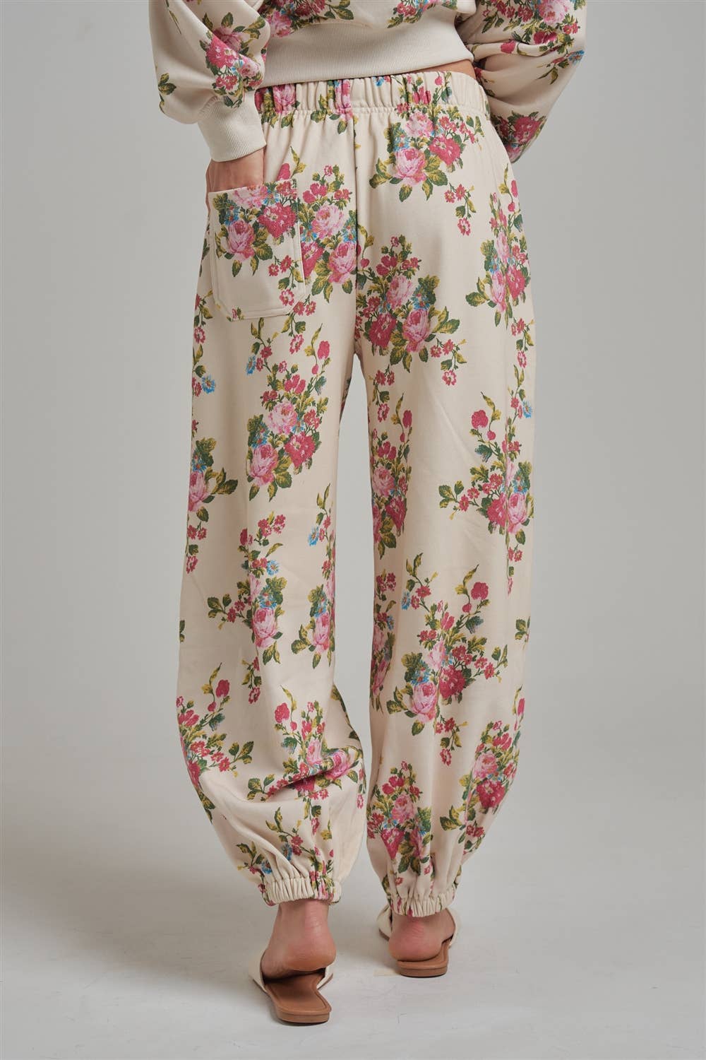 Floral patterned wide leg jogger sweat pants worn by a person with white sandals facing a plain background