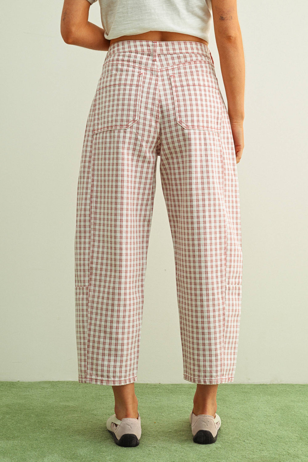 Person wearing pink and white checkered barrel pants facing a green and beige background