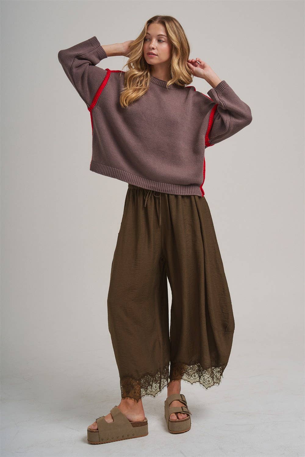 Woman wearing a brown sweater and wide-leg pants with lace trim on a plain background