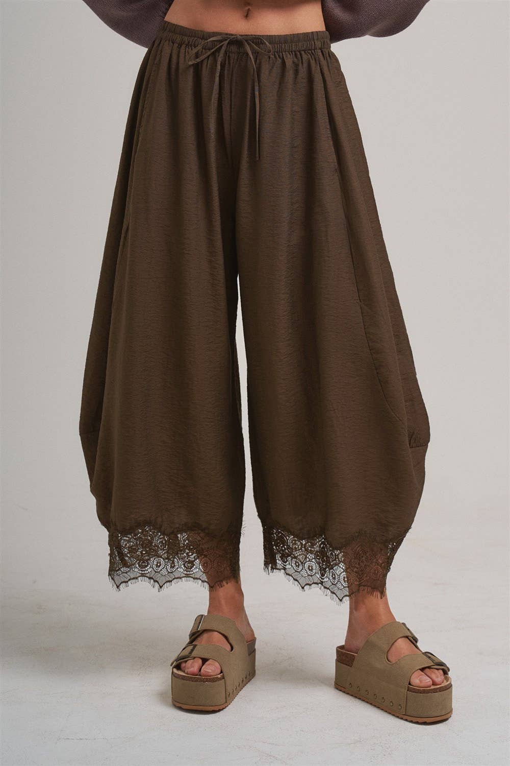 Brown wide-leg pants with lace trim worn by a person also wearing platform sandals on a plain background